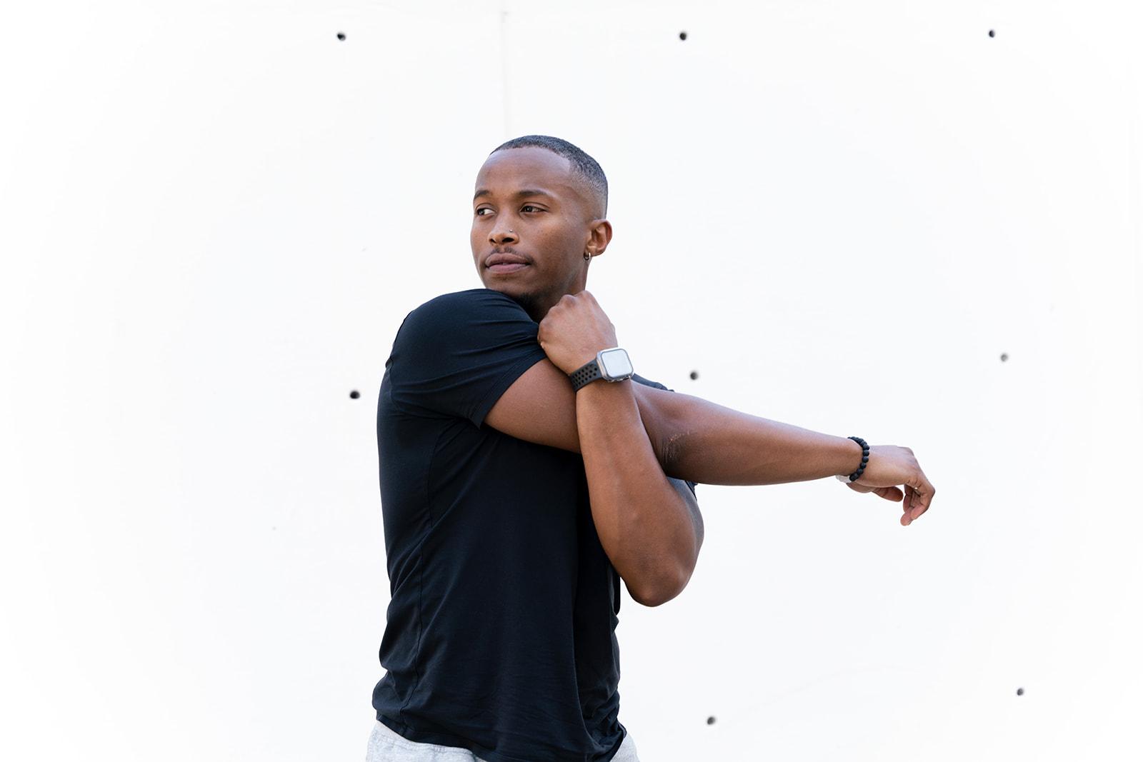 Coach Jaalen Jones stretching his shoulder in a black t-shirt